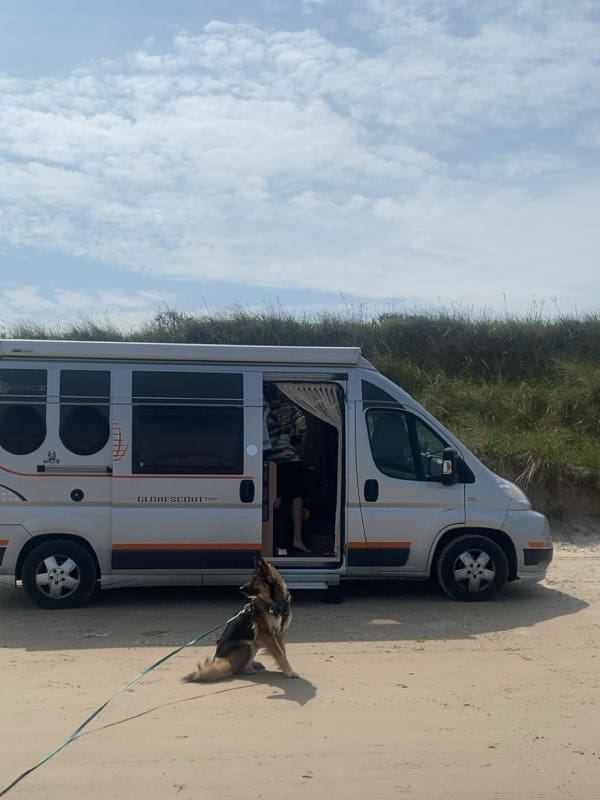 Leeyah sitzt am Strand vor dem Camper